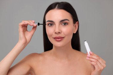 Gri arka planda kirpiklerine serum süren güzel bir kadın. Kozmetik ürünü