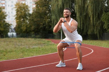 Stadyumda elastik direniş bandıyla egzersiz yapan kaslı adam.