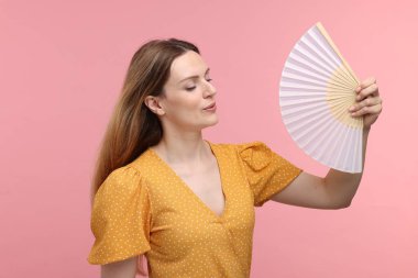Pembe arka planda serinlemek için sarı yelpaze sallayan güzel bir kadın.