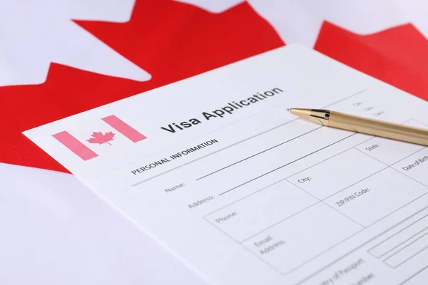 Immigration to Canada. Visa application form and pen on flag, closeup