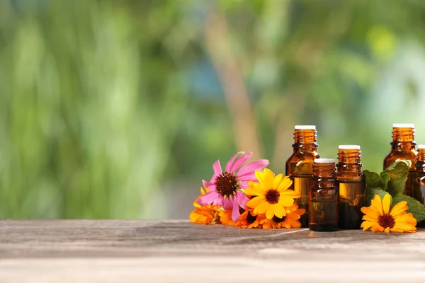 Bottles with essential oils, mint and flowers on wooden table against blurred green background. Space for text