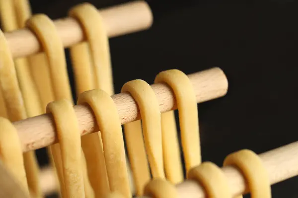 Homemade pasta drying on wooden rack against dark background, closeup