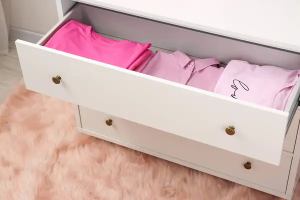 Many folded pink clothes in white chest of drawers indoors