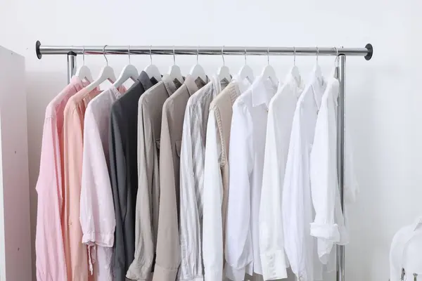 Rack with different stylish shirts near white wall. Organizing clothes