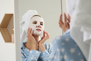 Yüzü maskeli genç bir kadın içeride aynaya bakıyor. Spa tedavileri