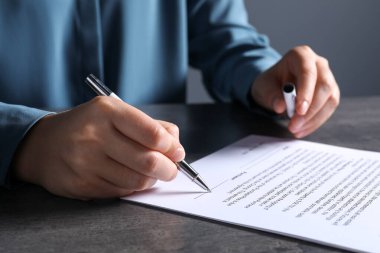 Gri masada kalemle belge imzalayan kadın, yakın plan