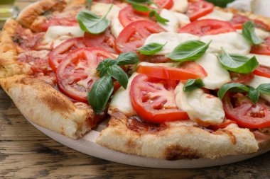 Domatesli lezzetli Caprese pizzası, ahşap masada mozzarella ve fesleğen, yakın plan.