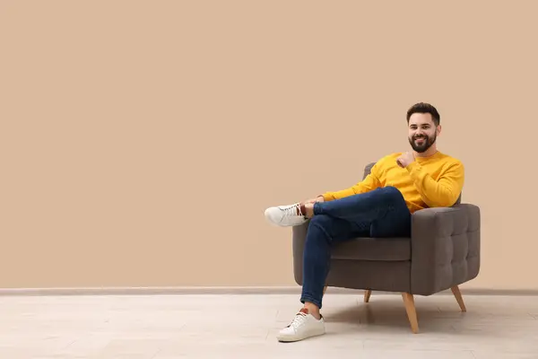 Handsome man sitting in armchair near beige wall indoors, space for text
