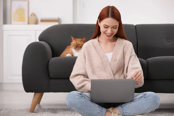 Happy woman working with laptop near cat on sofa at home