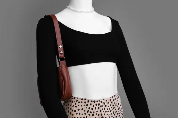 Female mannequin with necklace and bag dressed in stylish outfit on grey background