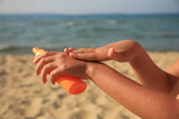Child applying sunscreen near sea, closeup. Sun protection care
