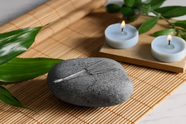 Stone with acupuncture needles and burning candles on table