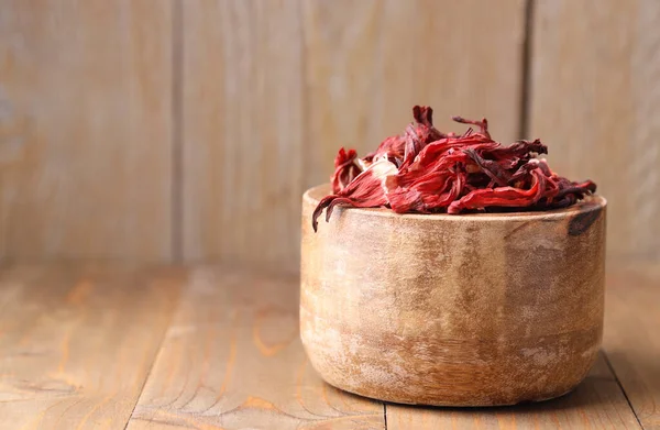 Dry hibiscus tea in bowl on wooden table, space for text
