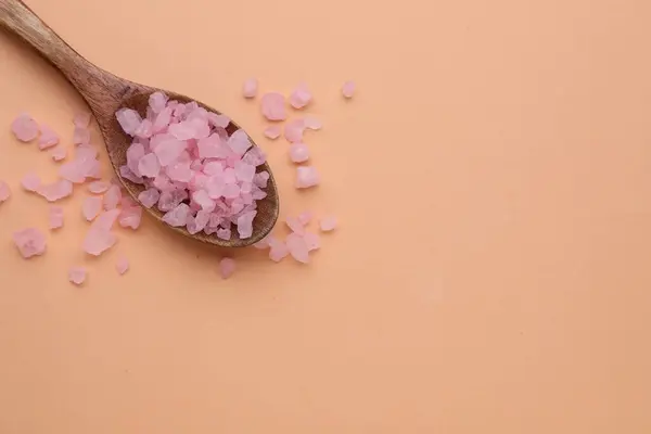 Spoon with pink sea salt on beige background, top view. Space for text
