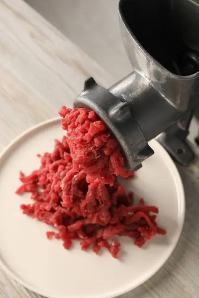 Metal meat grinder with beef mince on light wooden table, above view