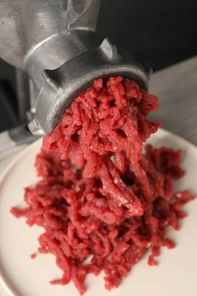 Mincing beef with metal meat grinder on light table, closeup