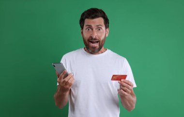 Akıllı telefonlu şok adam ve yeşil arka planda kredi kartı. Dikkatli ol, sahtekar.