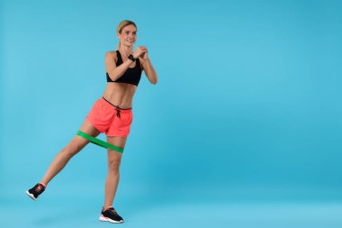 Açık mavi arka planda elastik direnç bandıyla egzersiz yapan bir kadın. Metin için boşluk