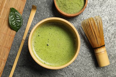 Cup of fresh matcha tea, bamboo whisk, spoon and green powder on grey table, flat lay clipart