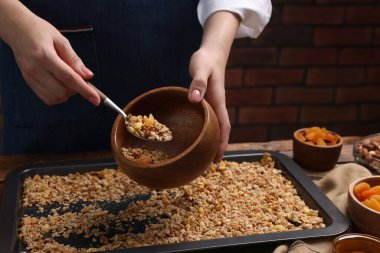 Bir kadın yemek tepsisinden kaseye granola koyuyor, yakın plan.