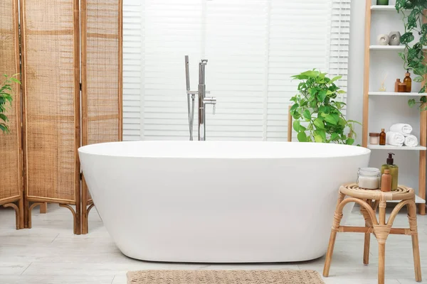 Spa day. Stylish bathroom interior with ceramic tub and green houseplants