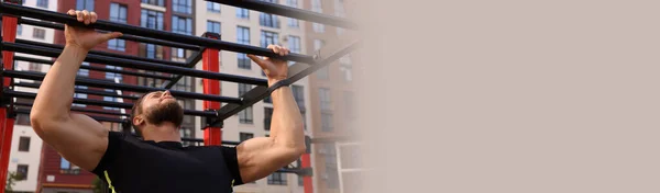 Man training on monkey bars at outdoor gym, space for text. Banner design