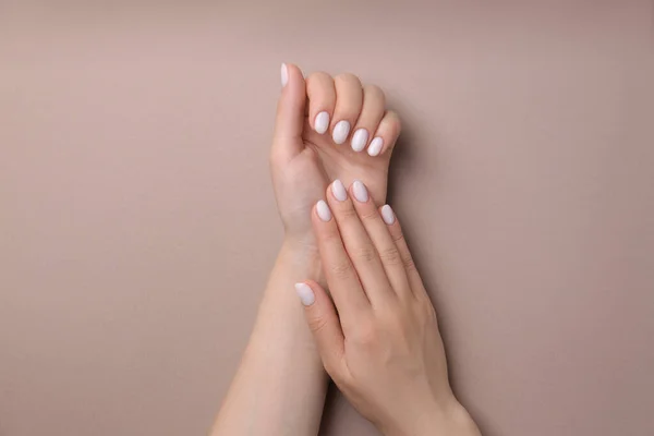 Woman showing her manicured hands with white nail polish on light brown background, top view