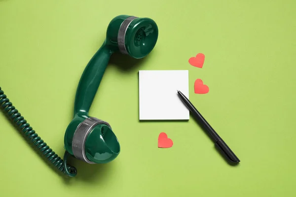 Long-distance relationship concept. Telephone receiver, empty note, paper hearts and pen on light green background, flat lay. Space for text