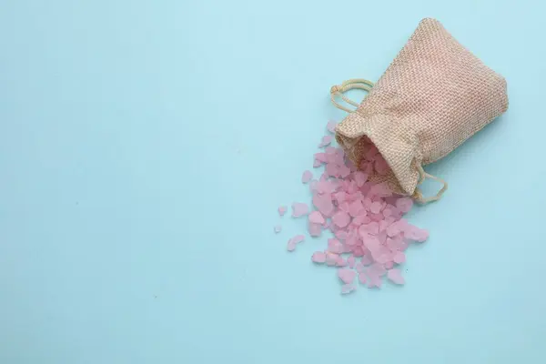 Bag with pink sea salt on light blue background, top view. Space for text
