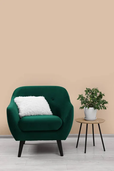 Stylish armchair and side table with plant near beige wall indoors