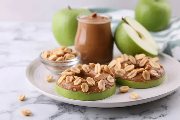 Fresh green apples with peanut butter and nuts on white marble table, closeup