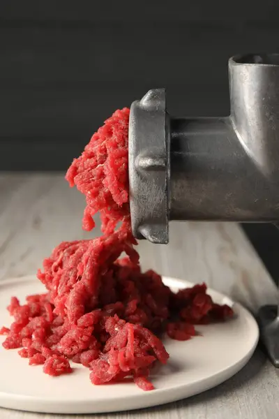 Mincing beef with metal meat grinder on light wooden table, closeup