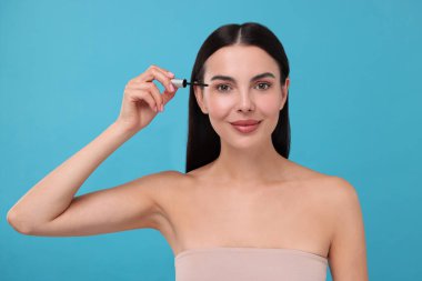 Kirpiklerine açık mavi arka planda serum süren güzel bir kadın. Kozmetik ürünü