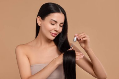 Güzel bir kadın bej arka plana saç serumu sürüyor. Kozmetik ürünü