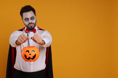 Korkunç vampir kostümü giymiş turuncu arka planda balkabağı kovası olan bir adam. Mesaj için yer var. Cadılar Bayramı