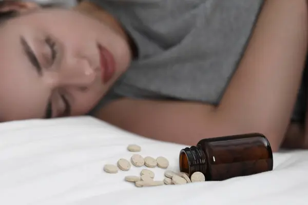 Depressed woman sleeping on bed near overturned bottle with antidepressants, selective focus