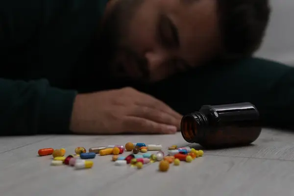 Man sleeping on floor, focus on overturned bottle with antidepressants
