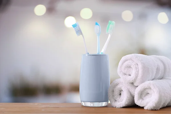 Plastic toothbrushes in holder on wooden table against blurred background, space for text