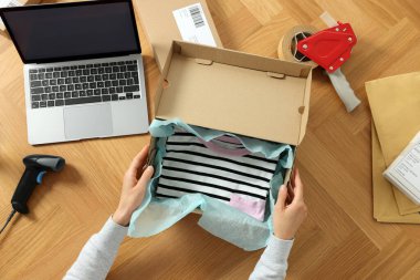 Ahşap masada giysi paketleyen bir kadın, üst manzara. Çevrimiçi mağaza