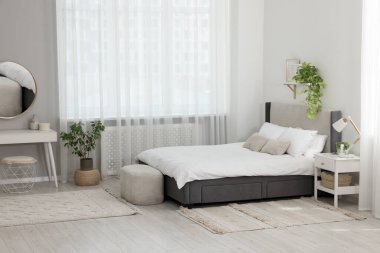 Şık bir yatak odası, geniş konforlu bir yatak ve pencerenin yanında bir şilte.