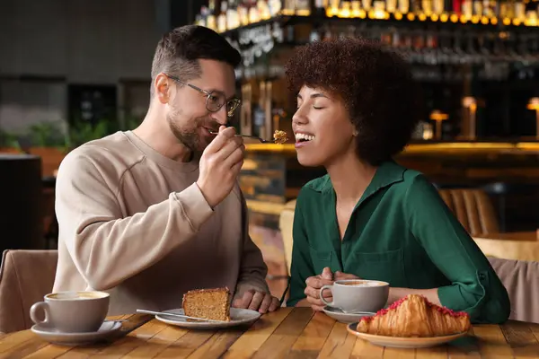International dating. Handsome man feeding his girlfriend with cake in cafe