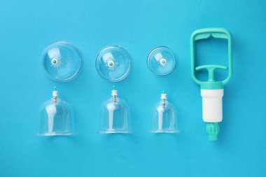 Plastik bardaklar ve el pompası açık mavi arka planda, düz yerde. Fincan terapisi.