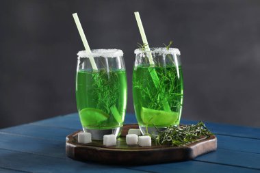 Mavi ahşap masada ev yapımı taze tarhun içeceği, filizler ve şeker küpleri.