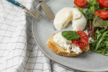 Domatesli burrata peyniri, roka ve tost kareli masa örtüsünde servis edilir, yakın plan.