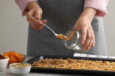 Gri masada yemek tepsisinden kavanoza granola koyan kadın, yakın plan.
