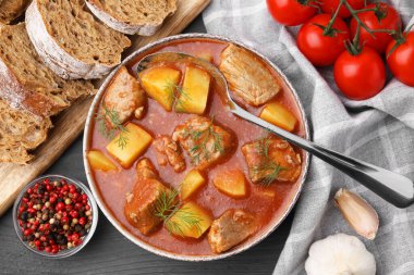 Lezzetli gulaş kasede, ekmek ve malzemeler koyu ahşap masada, düz yerde.