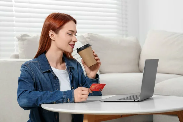 Happy woman with credit card near laptop at home, space for text. Online shopping