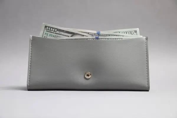 Stylish leather purse with dollar banknotes on light grey background