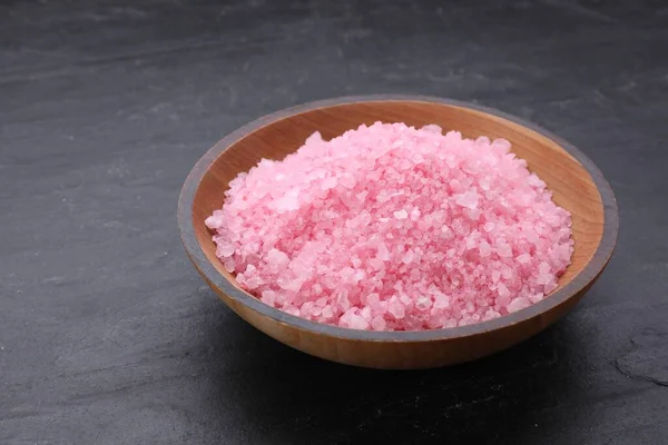 Bowl with pink sea salt on black table, closeup
