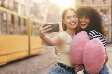 Pembe pamuk şekerli mutlu arkadaşlar güneşli bir günde şehirde selfie çekiyorlar. Metin için boşluk